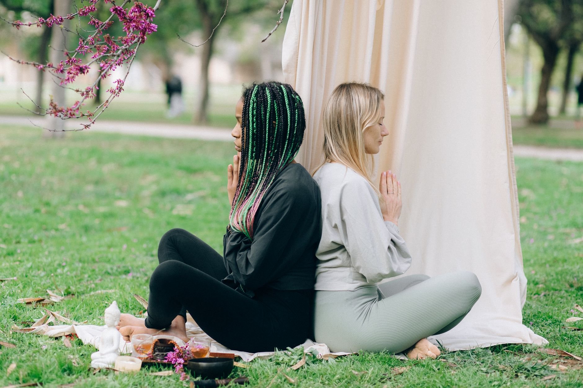 Two women meditating back-to-back in a serene outdoor setting.